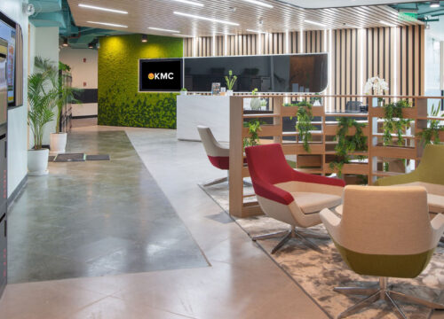 Modern KMC coworking office lobby with lounge seating, moss wall, smart lockers, and branded digital signage screens.