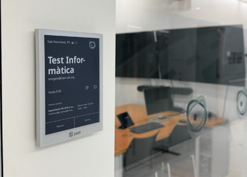 Joan e-ink display mounted outside a meeting room showing a current booking for 'Test Informàtica' with schedule details.