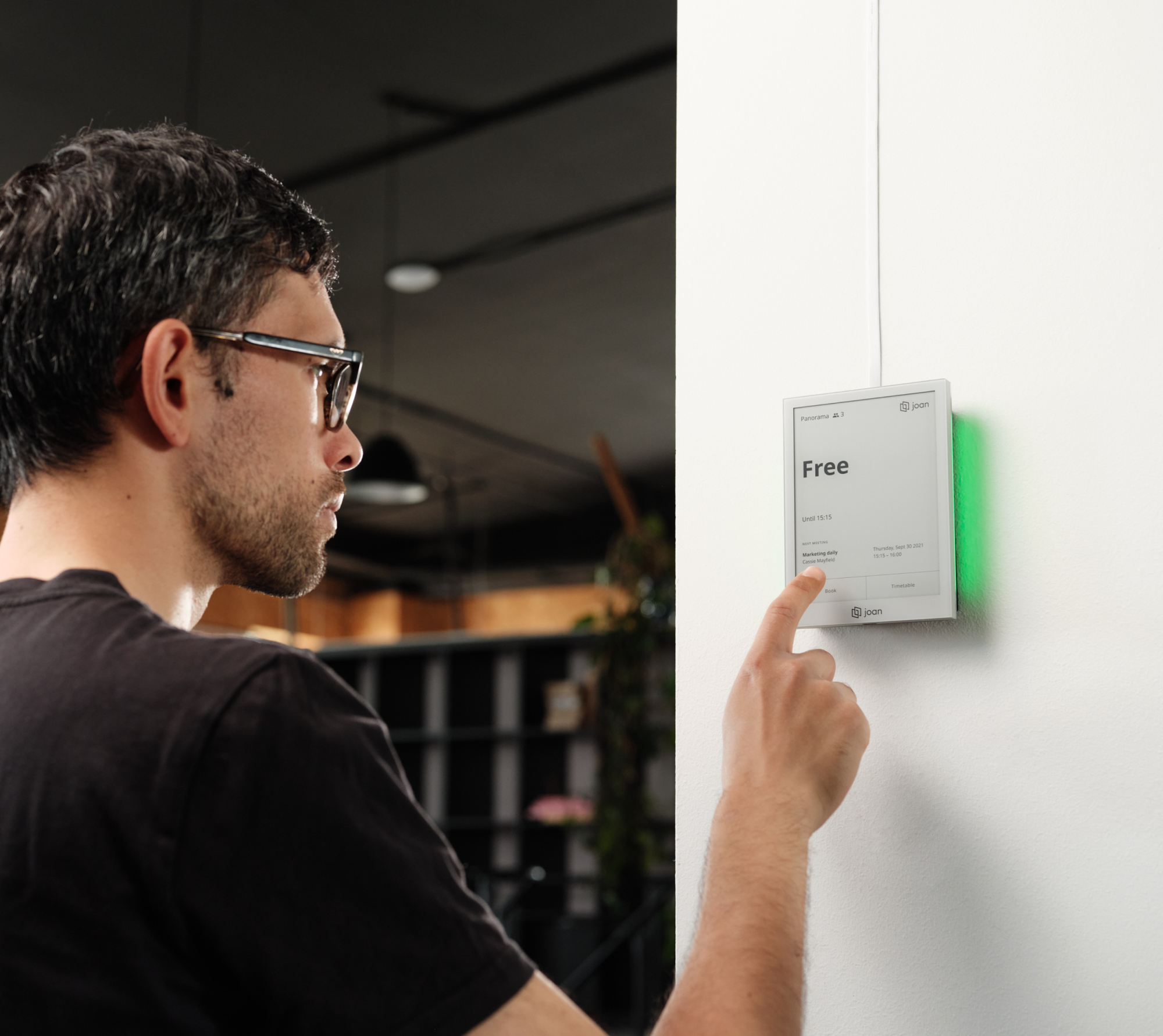 A person tapping a wall-mounted Joan 6 Pro that shows Free, with the mount glowing green beside it.