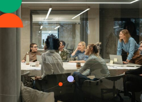 Team of colleagues collaborating in a modern glass-walled meeting room with laptops and documents on the table.