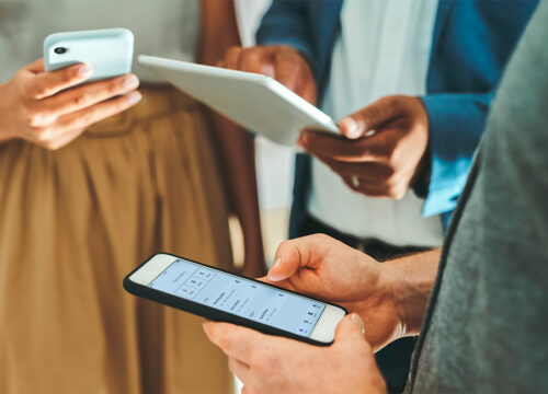 Three professionals using smartphones and a tablet to manage workplace tasks with a workspace management app.