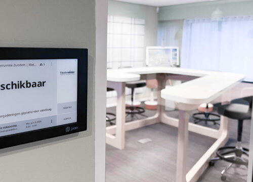 Joan 13 e-ink display mounted outside a meeting room showing 'Beschikbaar' with Thuisvester branding