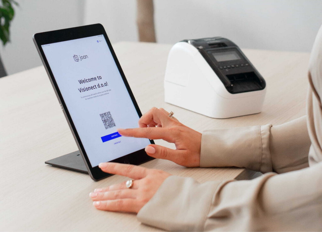 Woman checking in via Joan visitor management app on a tablet beside a badge printer.