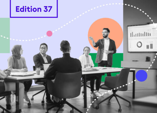 Diverse team in a meeting room watching a presenter beside a data dashboard screen — Joan Magazine Edition 37.
