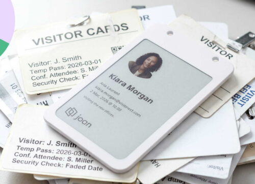 Joan e-paper visitor badge displaying Kiara Morgan's details, resting on a pile of traditional paper visitor cards.
