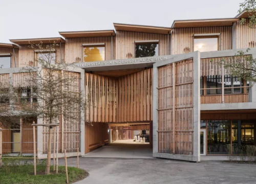 Exterior of Universitäts-Kinderspital Zürich, featuring a timber-clad facade and arched entrance by Herzog & de Meuron.