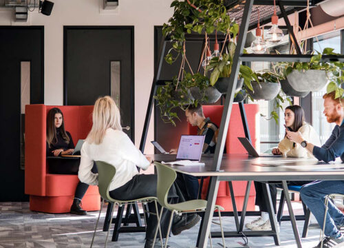 Four colleagues collaborating at a table in Pax8's modern office with biophilic design and bright furniture.