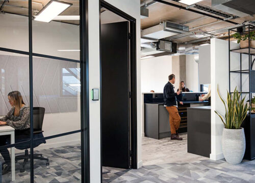 Private meeting room with crittall glass walls in a modern office, woman working on laptop inside.