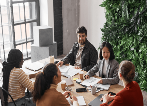 Diverse team of five professionals collaborating around a wooden table in a modern office with a green living wall.