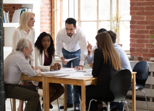 Diverse team of professionals collaborating around a meeting table in a modern office with brick walls.