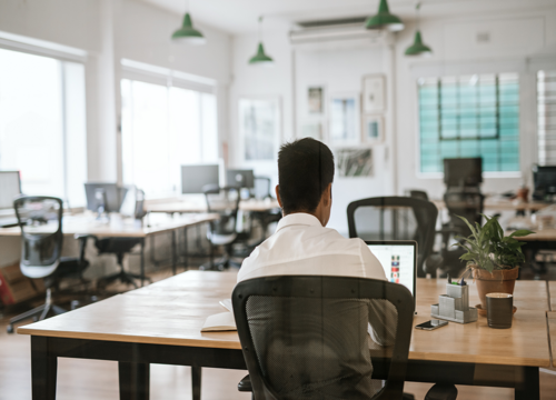 Person working alone at a wooden desk in a largely empty modern open-plan office.
