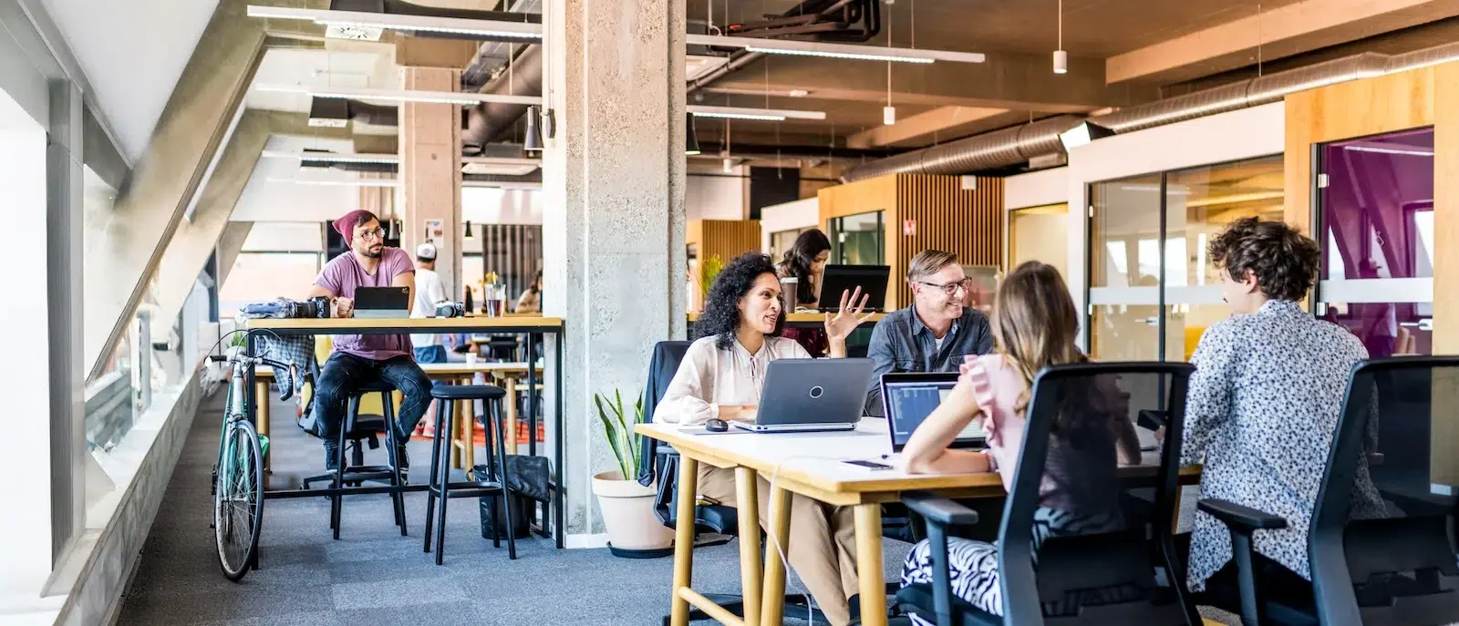 Diverse group of professionals collaborating around a laptop-filled table in a bright, modern coworking office space.