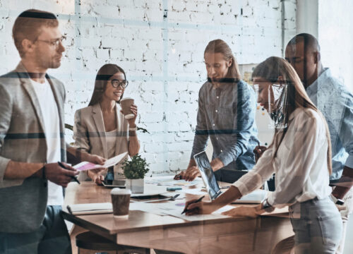 Diverse team of five professionals collaborating around a meeting table in a modern loft-style office.