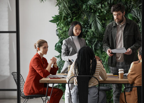 Diverse team of five professionals in a collaborative meeting inside a modern biophilic office with a green plant wall.