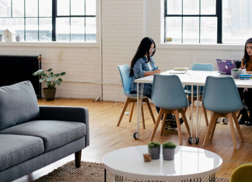 Two women working independently at a long white table in a bright, modern open-plan co-working space.