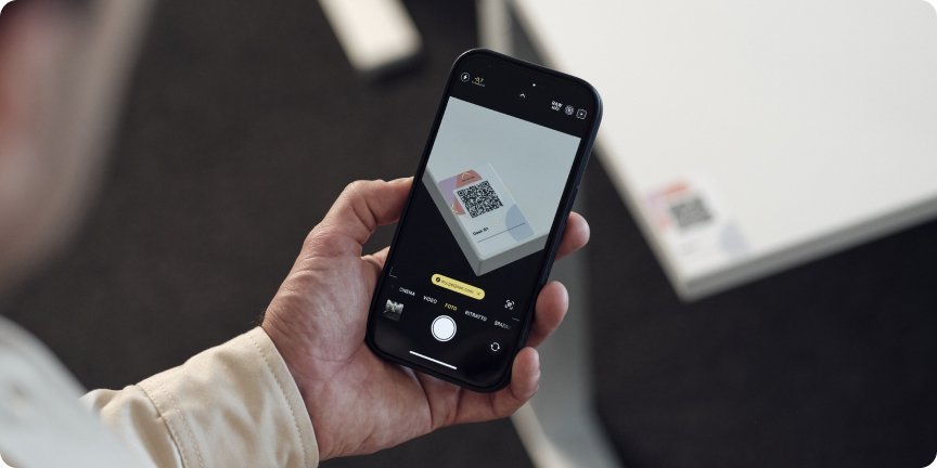 Person scanning a QR code on a Joan e-ink display using a smartphone camera in an office setting.