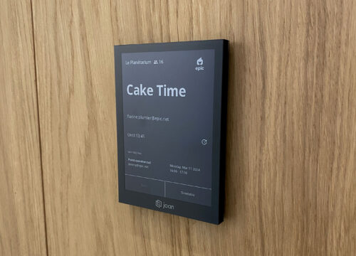 Joan 6 Pro e-ink display mounted on a wood wall showing the 'Cake Time' meeting in room Le Planétarium.