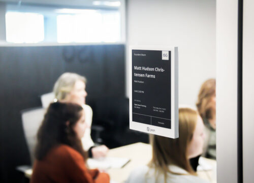 Joan 13 e-ink display mounted outside a conference room showing ISG-branded meeting schedule and current booking.
