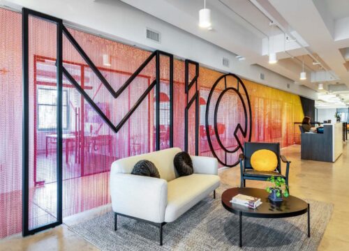 MiQ office lobby with colorful beaded letter wall installation, cream sofa, armchair, and coffee table in a modern workspace.