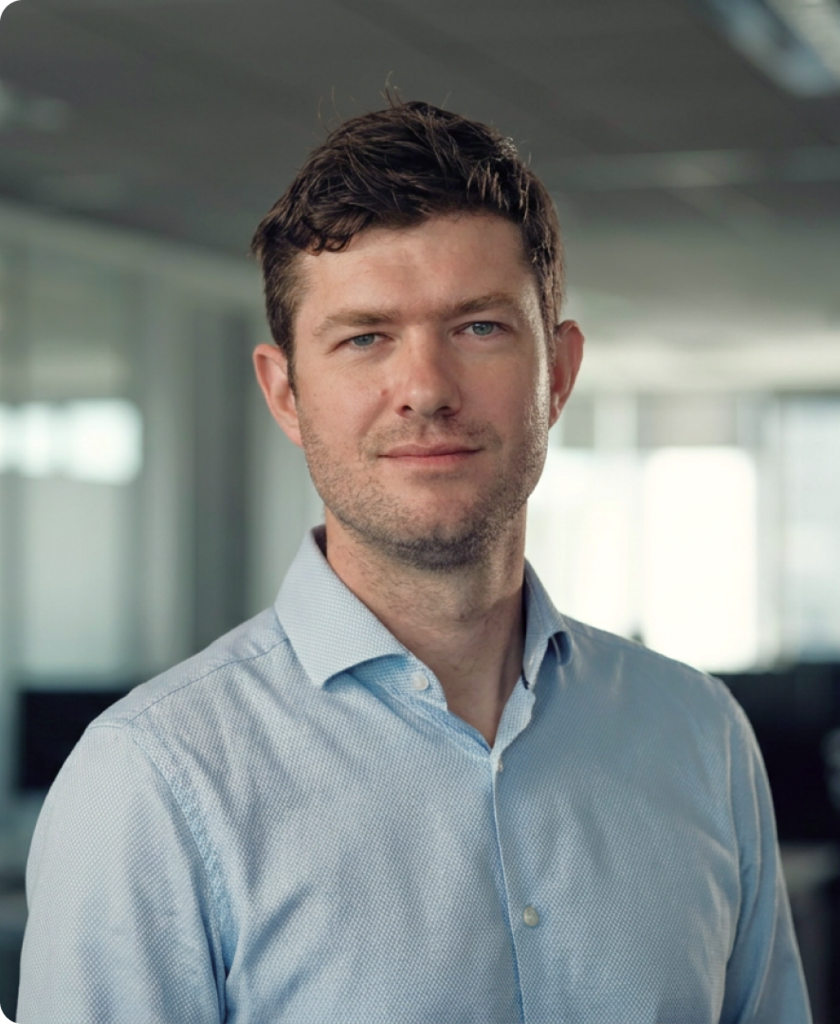 Professional headshot of a man named Rok in a light blue shirt, photographed in a modern office setting.