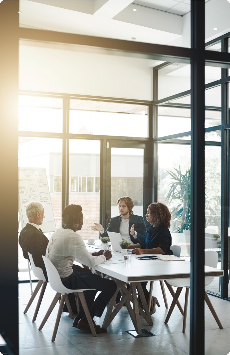 Four colleagues in a glass-walled conference room during a meeting.