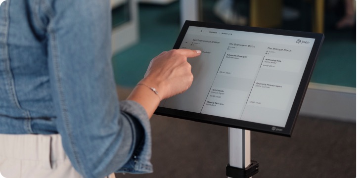 Person touching a Joan 13 e-ink display mounted beside a meeting room door.