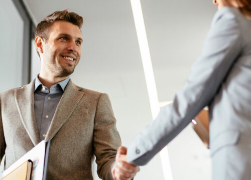 Two professionals shaking hands in a modern office, representing a welcoming visitor management experience.