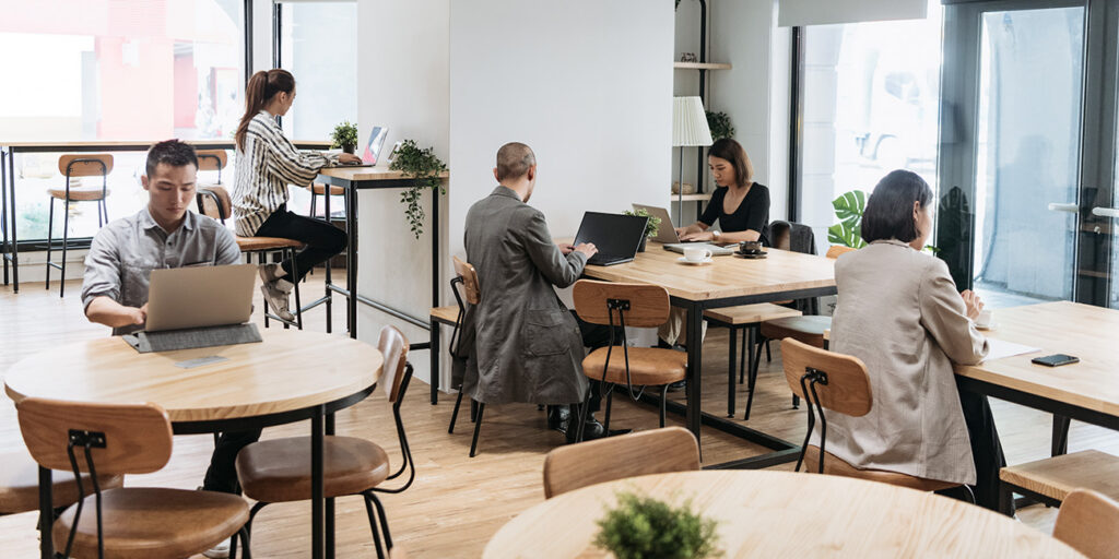Professionals working independently in a modern, bright coworking space with laptops and open desks.