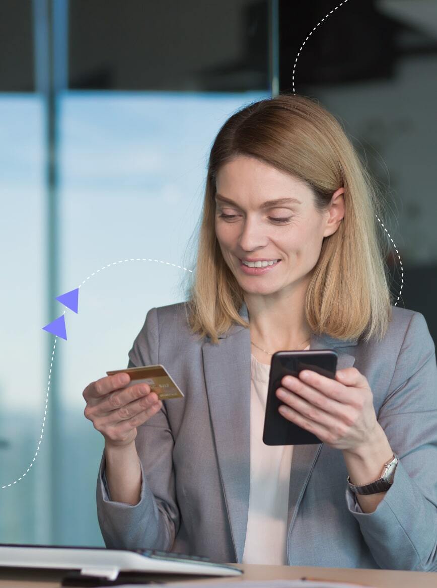 Woman in blazer using smartphone while holding a credit card, possibly calculating costs.