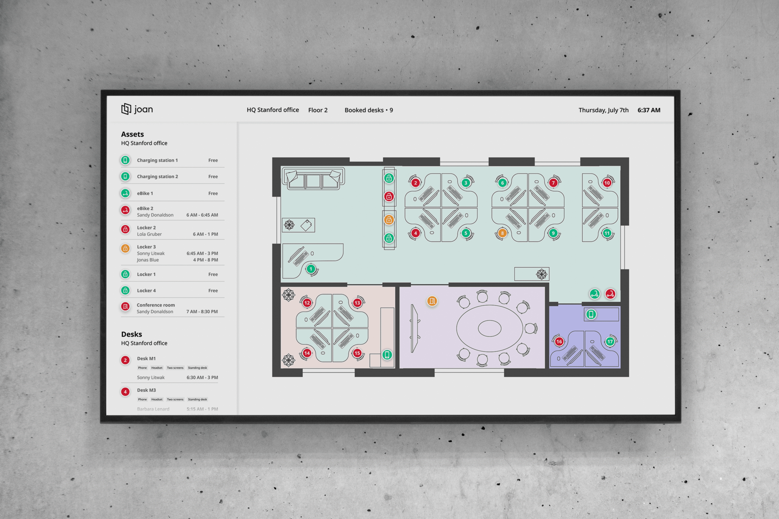 Wall-mounted TV display showing Joan floor plan with color-coded desk and asset availability for an office.