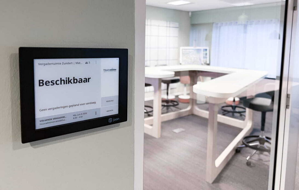 Joan 13 e-ink display mounted outside a meeting room showing 'Beschikbaar' (Available) with Thuisvester branding.