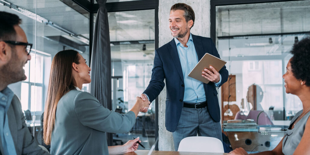 Business professionals shaking hands during a meeting in a modern office environment.