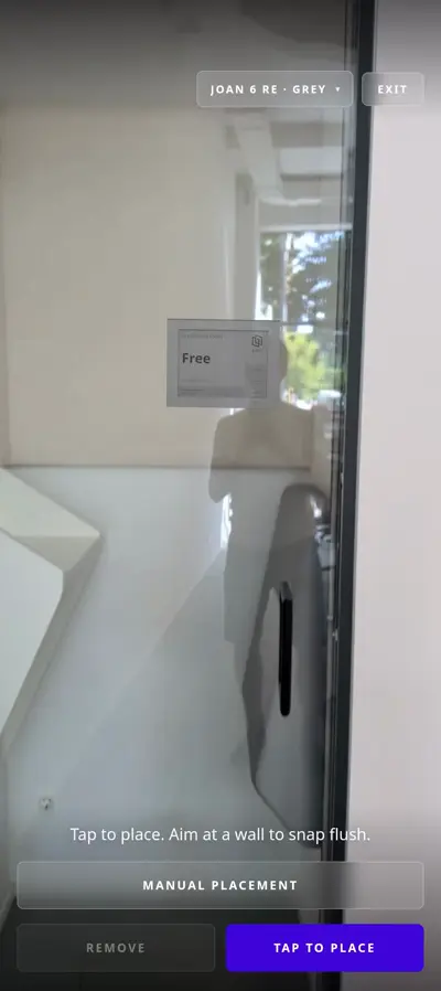 AR placement tool on a smartphone showing a Joan e-ink display previewed on a white office wall near a glass door.