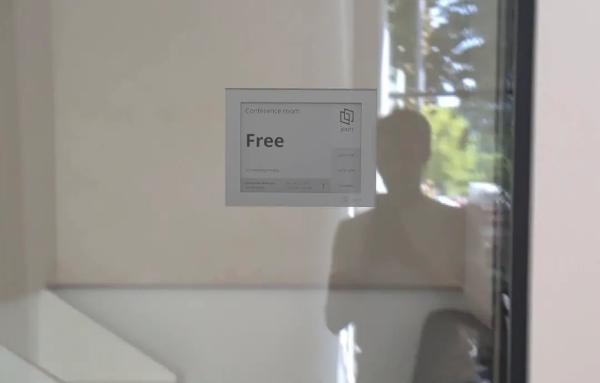 Joan e-ink display mounted on a glass office partition showing 'Free' room status.
