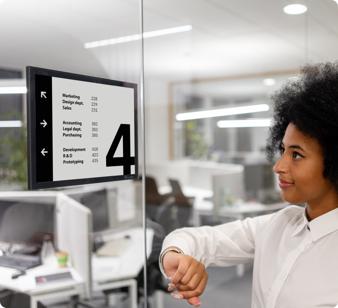 Woman interacting with a Joan 13 e-ink display showing a floor 4 office wayfinding directory with department room numbers.
