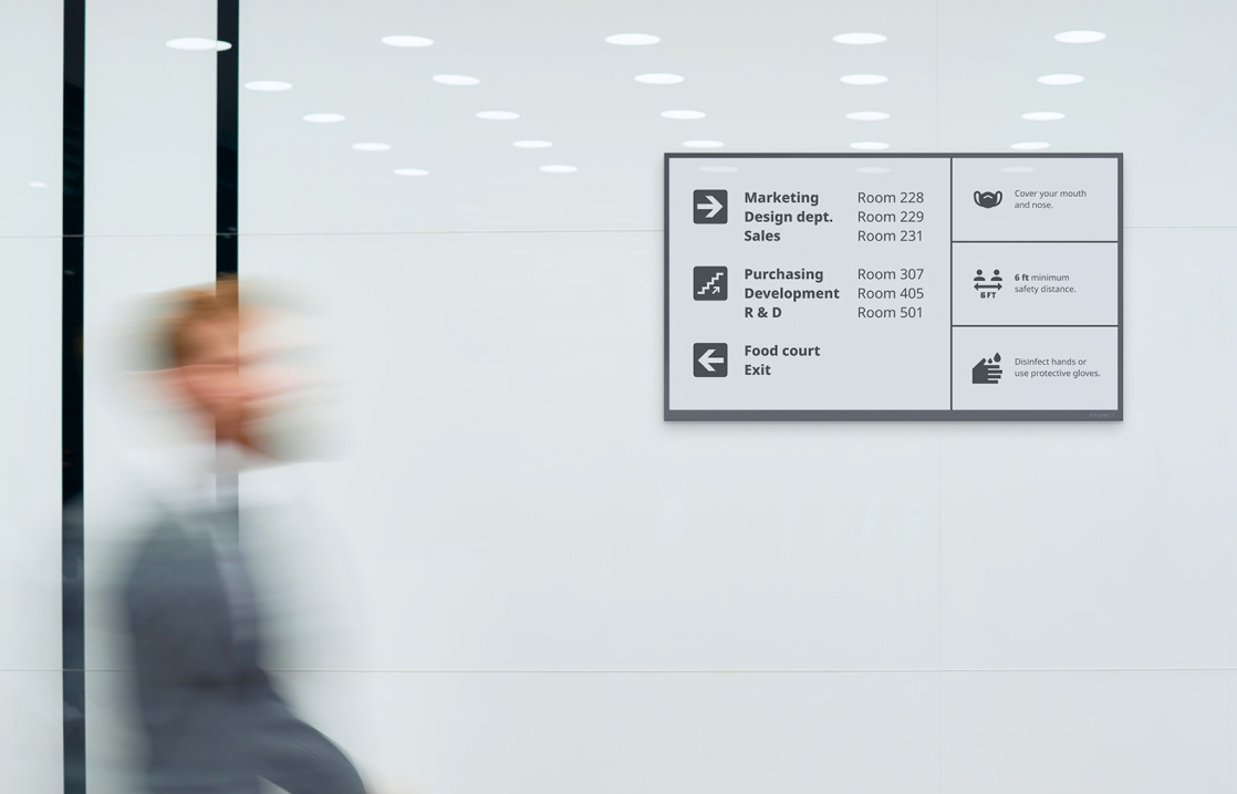 Digital signage display showing office wayfinding and health safety notices mounted on a white corridor wall.