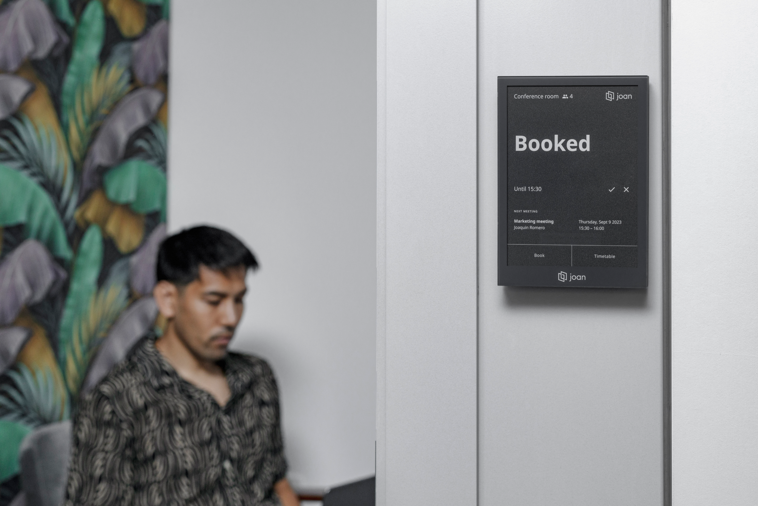 Joan 6 Pro e-ink display mounted outside a conference room showing a 'Booked' status until 15:30.